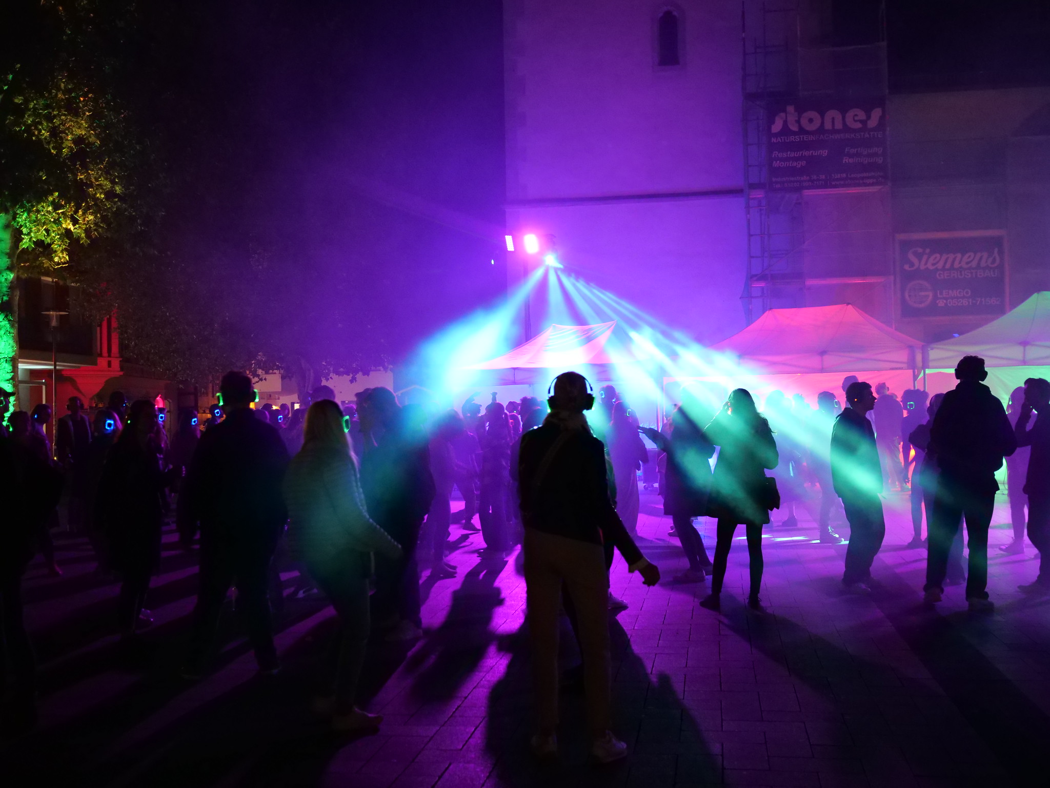 Mensen dansen met draadloze koptelefoons onder kleurrijke verlichting tijdens een silent disco evenement