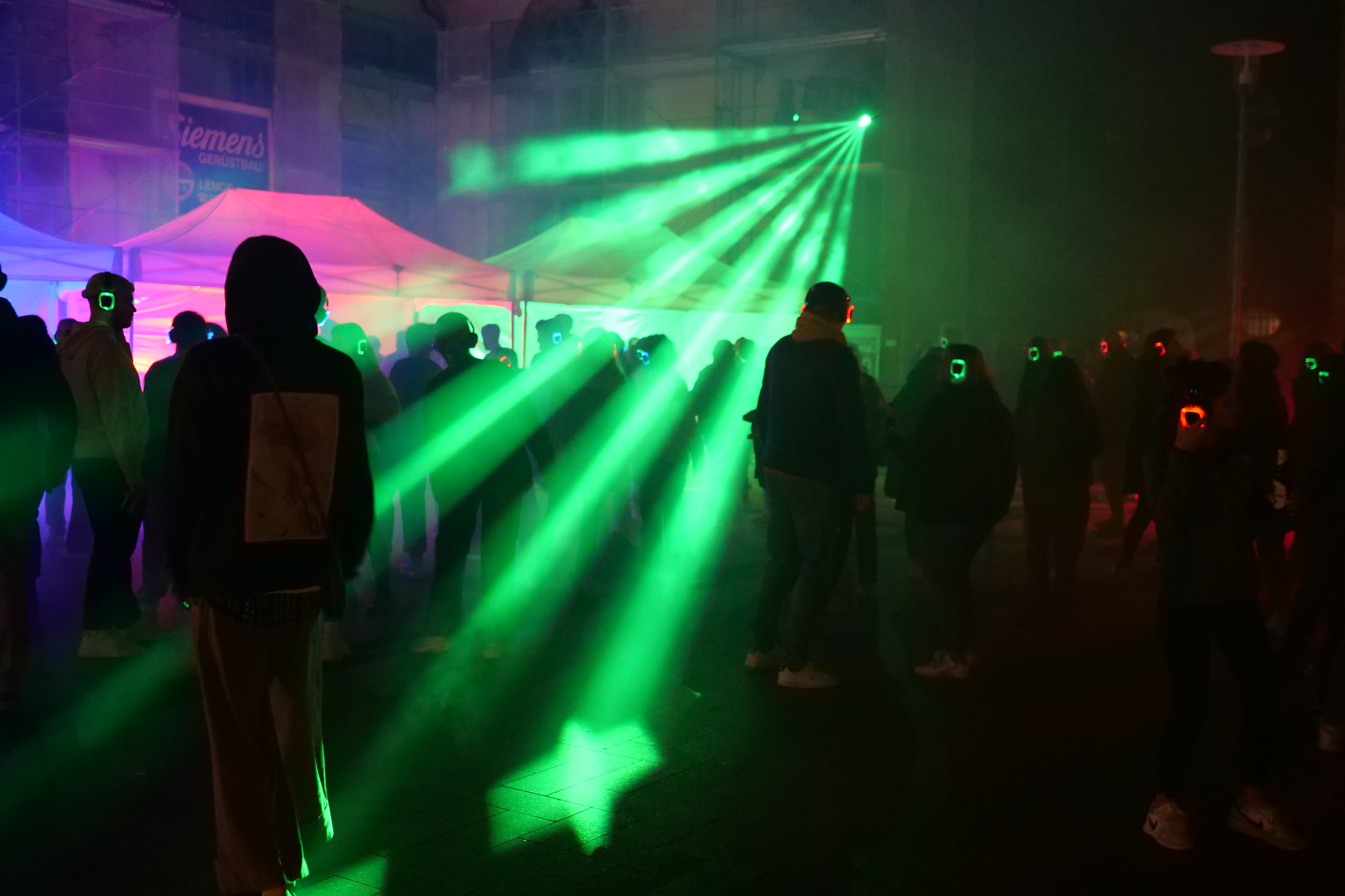Silhouetten van mensen dansen in groene laserverlichting tijdens een silent disco evenement