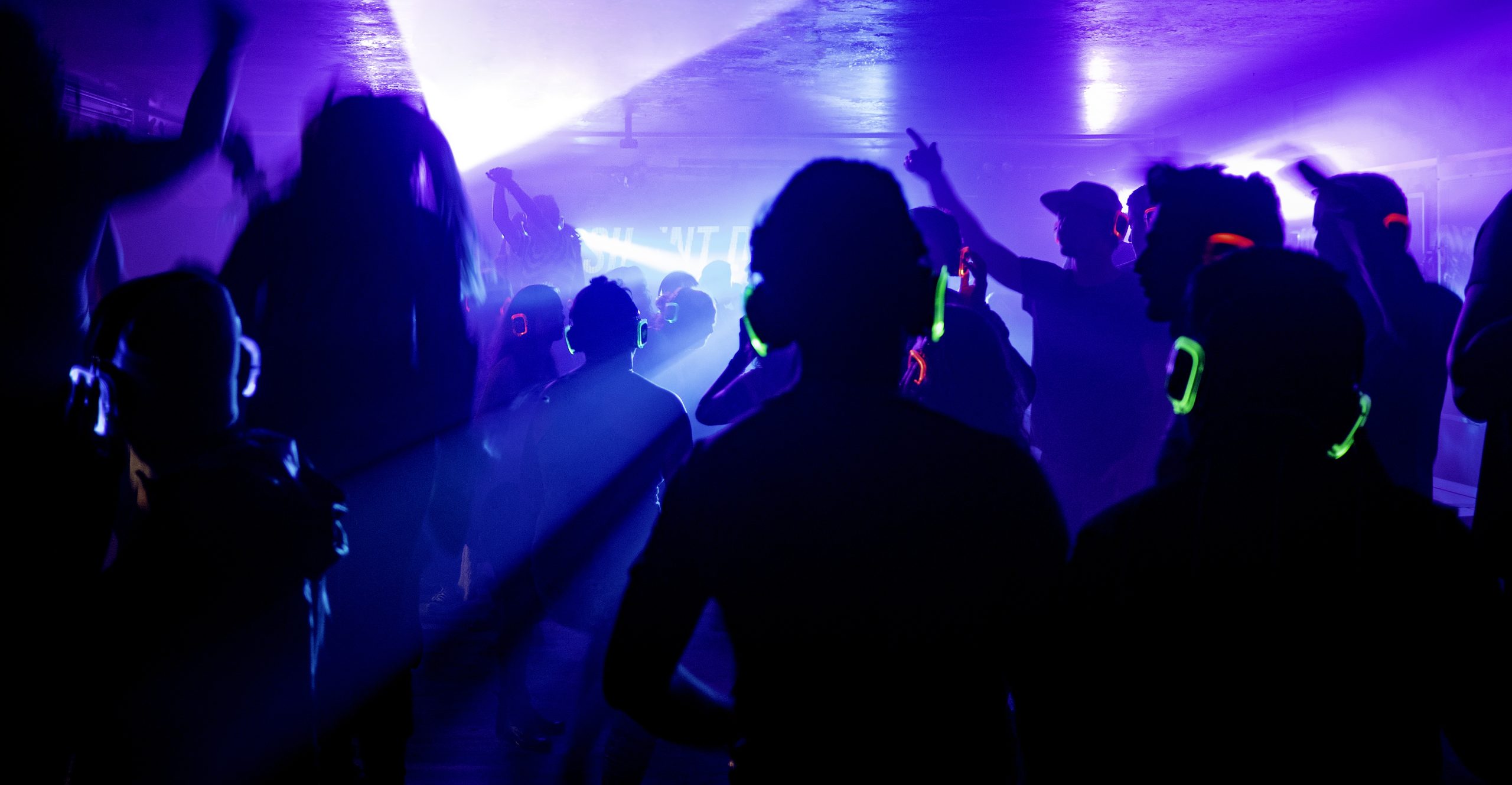 Menigte danst met draadloze koptelefoons onder paarse verlichting tijdens een silent disco feest